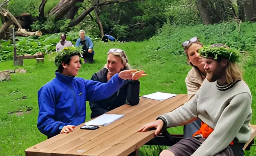 En gruppe mennesker sidder sammen ved et bord udendørs og taler sammen